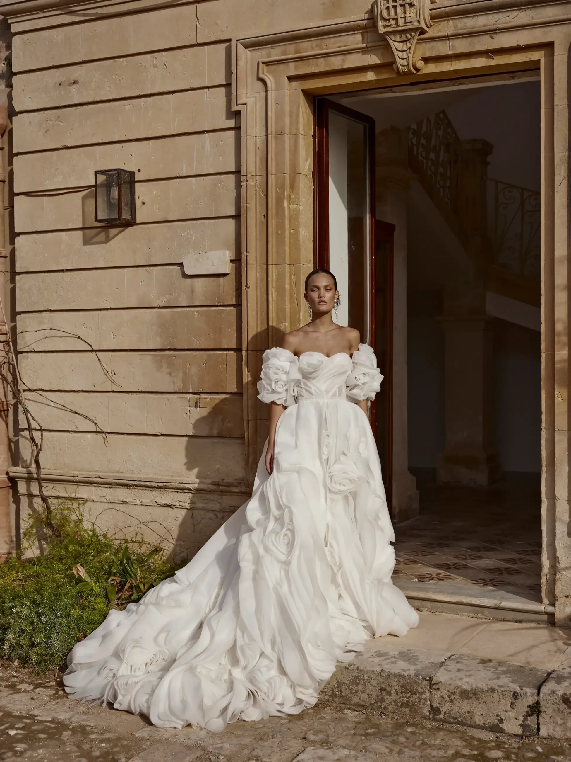 Model is wearing a textured gown adorned with oversized rosettes and 3D floral details for a sculptural, artistic look.