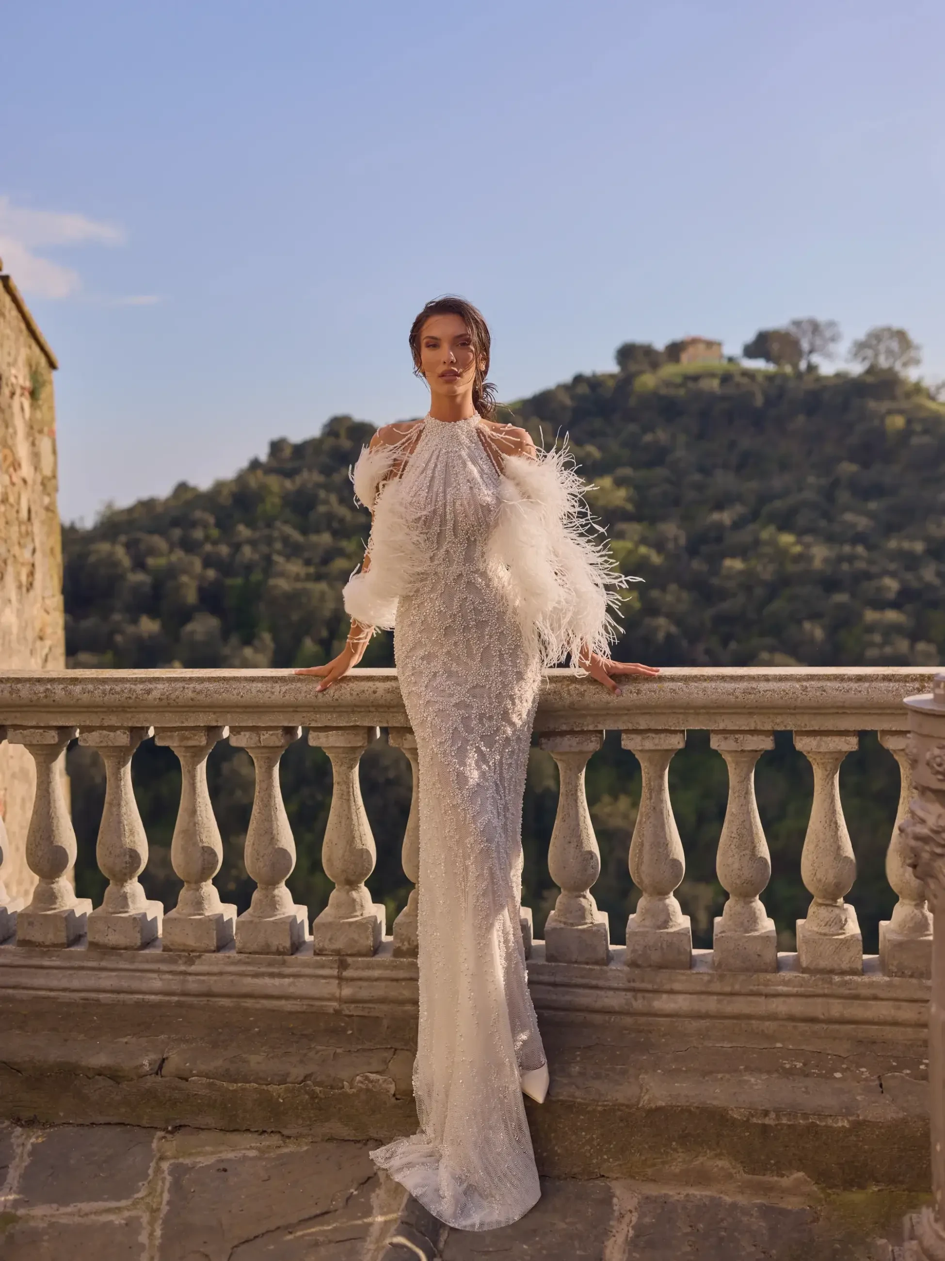 model is wearing a sleeveless wedding gown with feathers