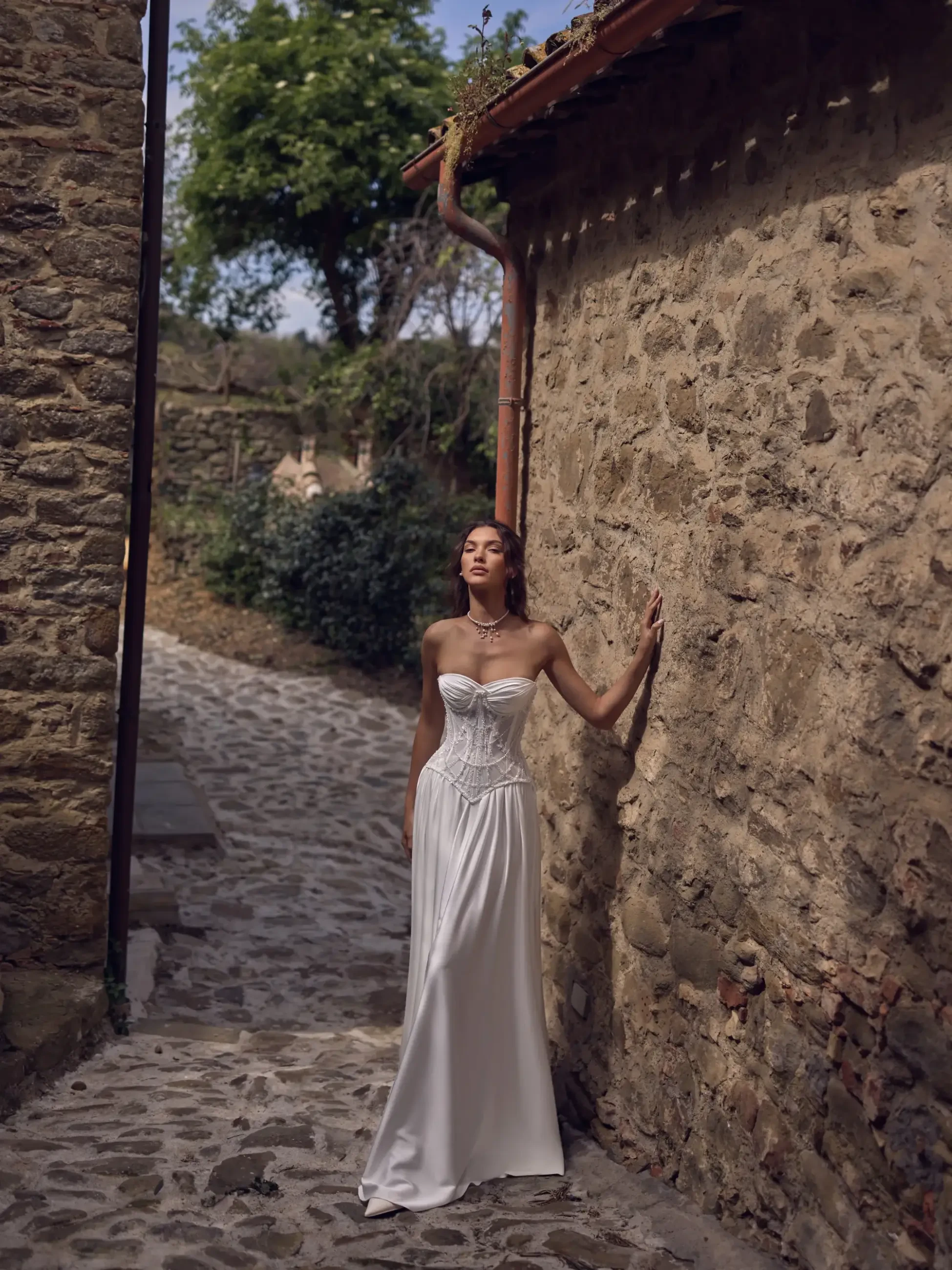 Model is wearing a romantic gown with a sheer lace-up corset and light silk skirt, styled with a removable lace overlay for two distinct bridal looks.