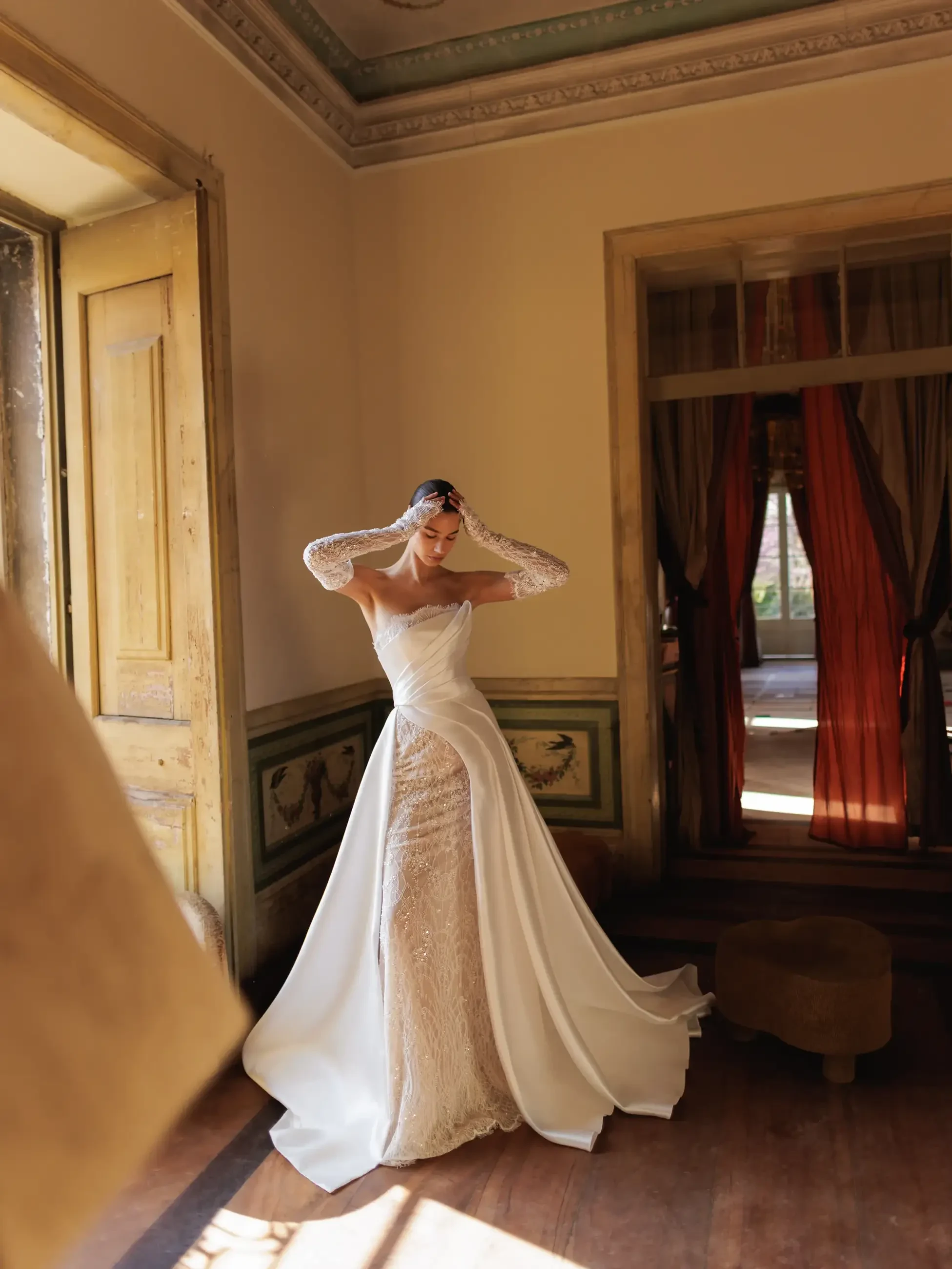 Model is wearing a beaded lace gown with a fitted silhouette, shown with an optional asymmetric overskirt and detachable wrap-top for multiple styling options.
